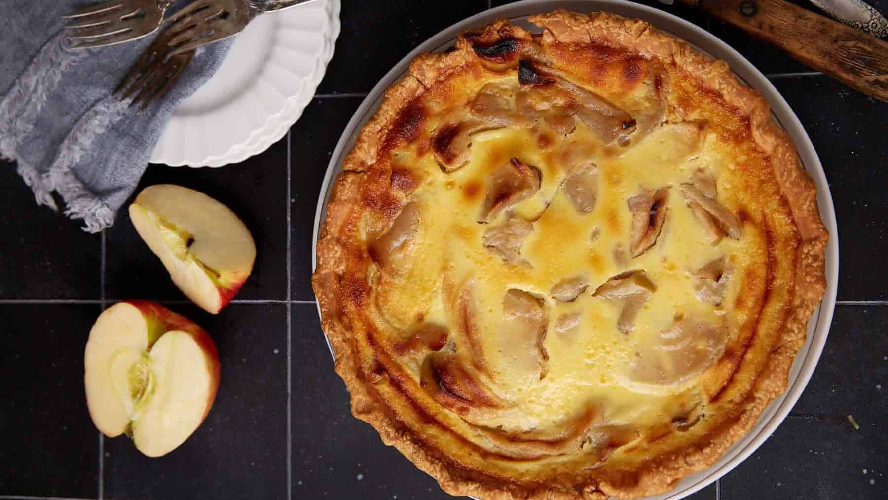 A fruit tart with a custard filling, next to apple slices and a fork.