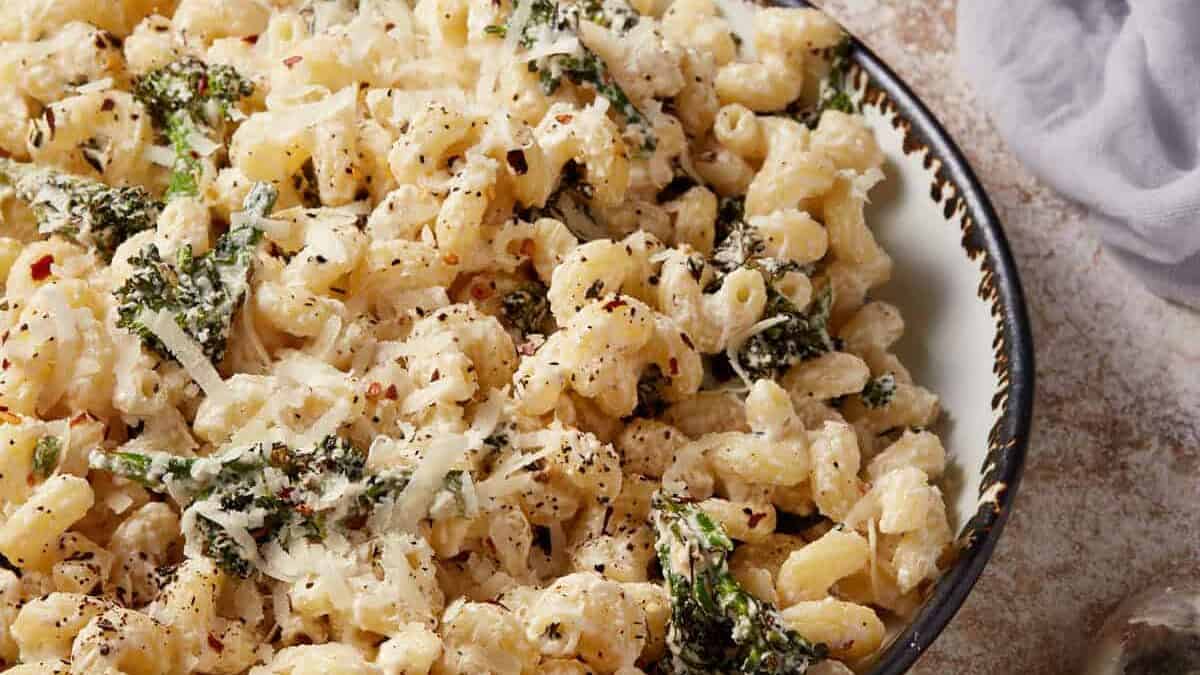 A bowl of creamy pasta with kale, topped with grated cheese and red pepper flakes.