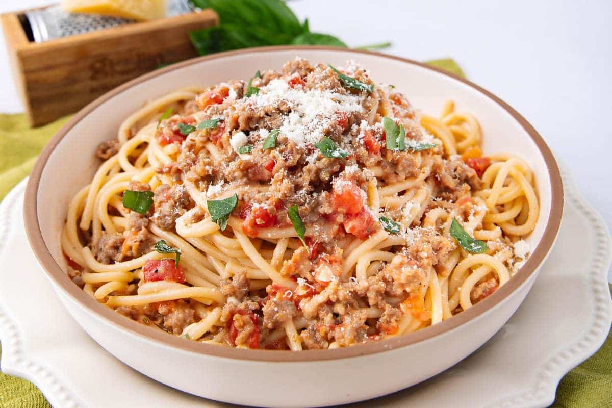 A bowl of spaghetti topped with meat sauce, herbs, and grated cheese.