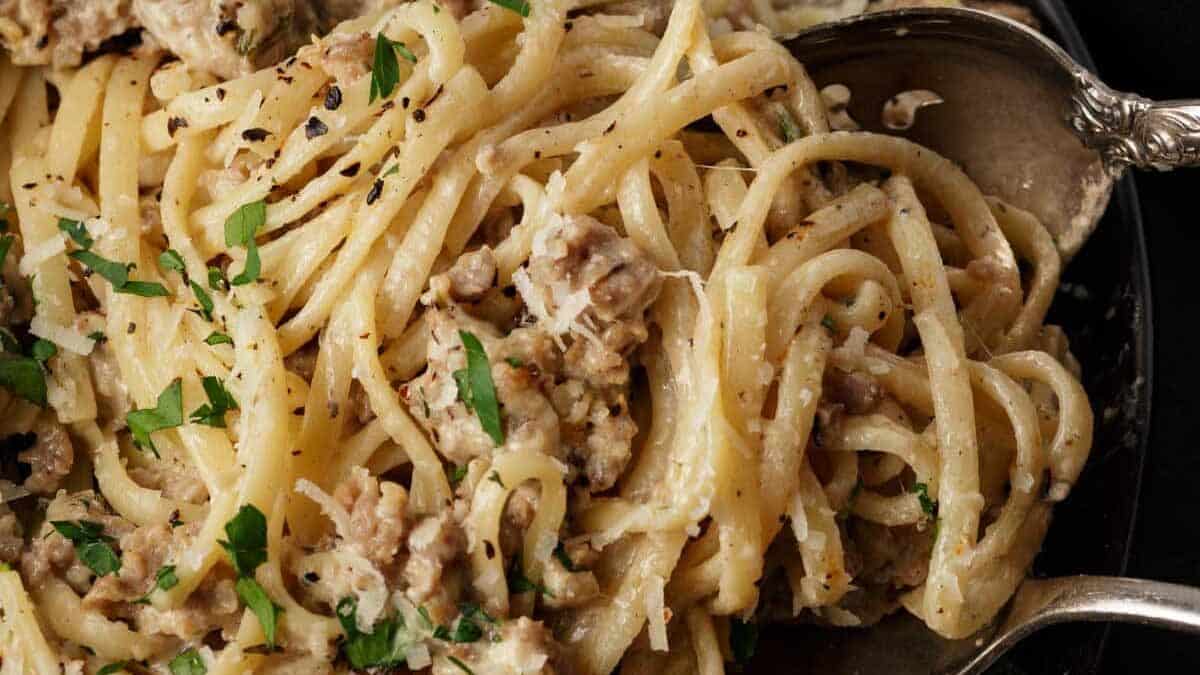 Linguine pasta with sausage and herbs in a creamy sauce, served in a bowl with a spoon.
