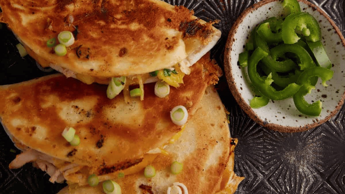 Golden-brown quesadillas topped with sliced green onions, served with a side of sliced jalapeños.